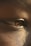 An extreme close-up of a person's eye, highlighting the texture of the skin around it and the details in the reflection on the eye surface. The lighting provides a warm tone, emphasizing the intricate details of the skin and eye.