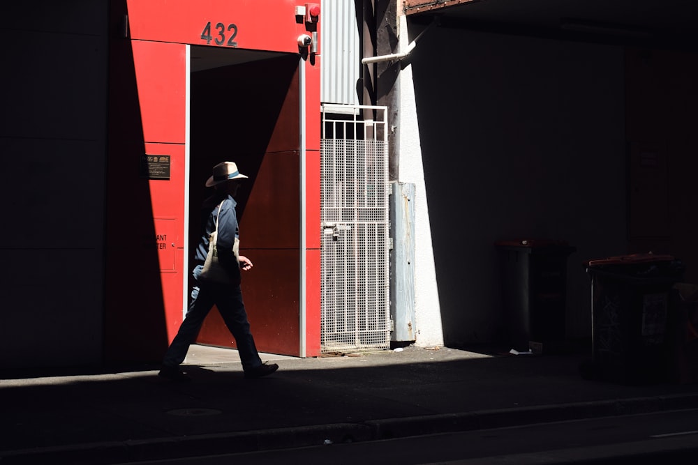 a man walking down a street past a red building
