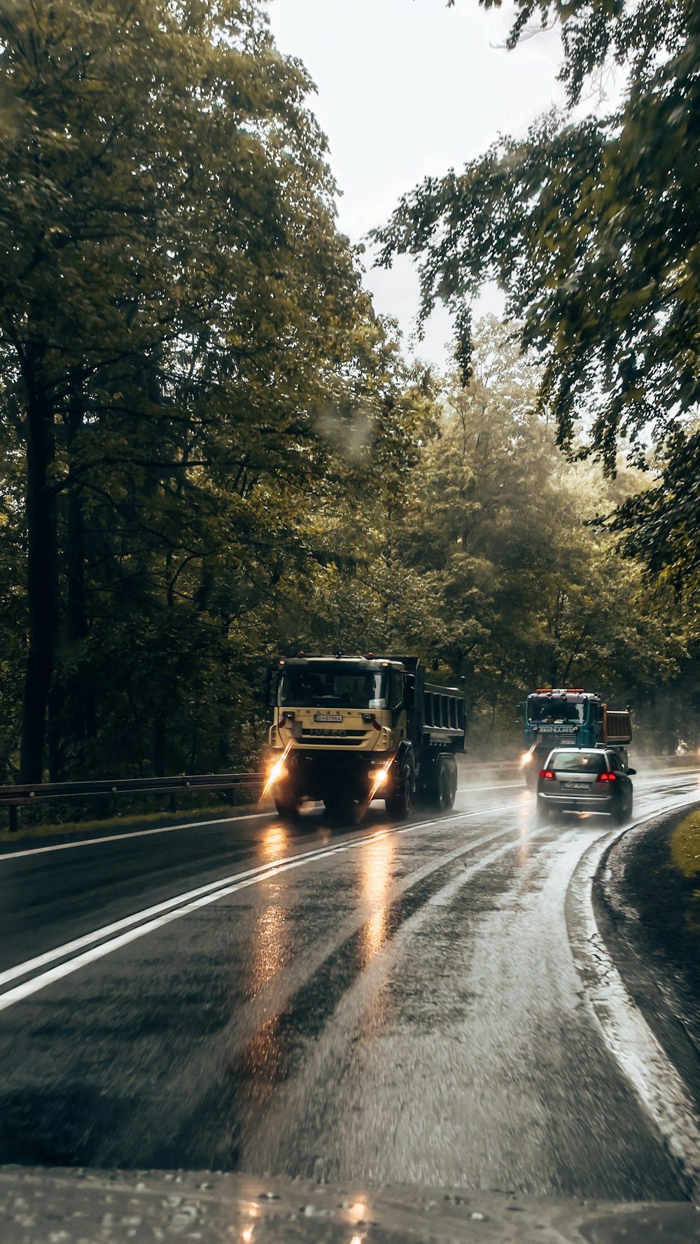 a couple of trucks driving down a rain soaked road