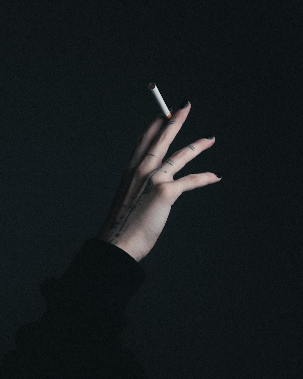 a woman's hand holding a cigarette in the dark