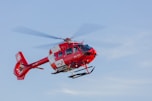 a red and white helicopter flying through a blue sky