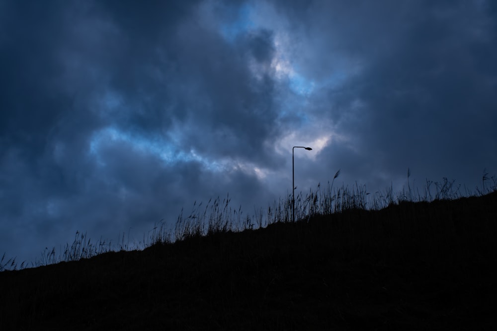 a street light sitting on top of a hill under a cloudy sky