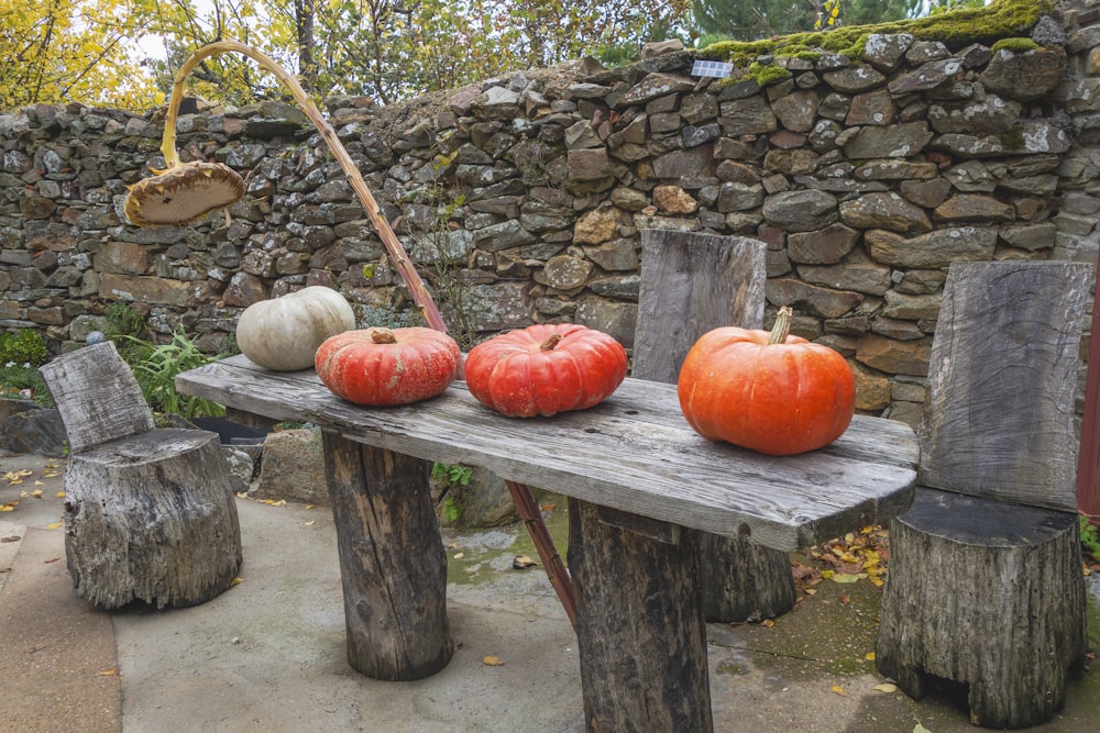 a wooden table topped with pumpkins next to a stone wall