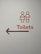 A minimalist toilet sign with stylized male and female figures in orange, accompanied by the word 'Toilets' and an arrow pointing to the left.
