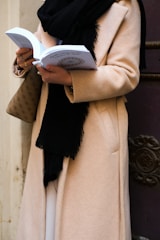 a woman in a beige coat is reading a book