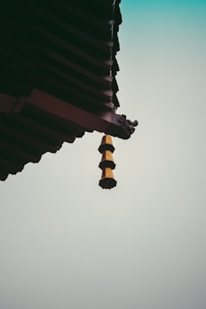 A traditional architectural roof corner with layered eaves and a decorative hanging ornament against a gradient sky.