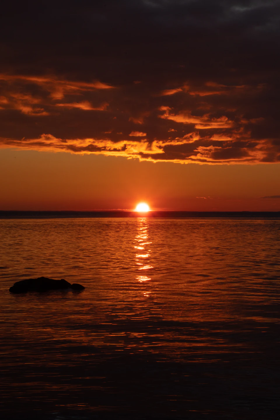 Sunset over calm waters with warm glow and reflected orange hues in foreground rocks