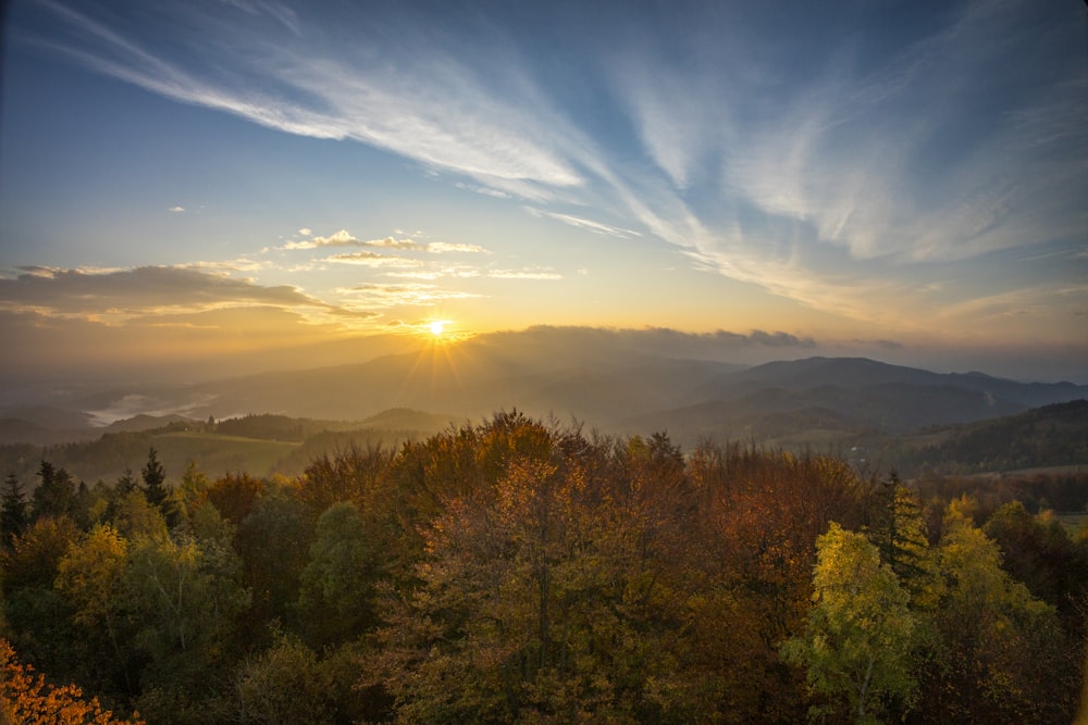 the sun is setting over the mountains and trees