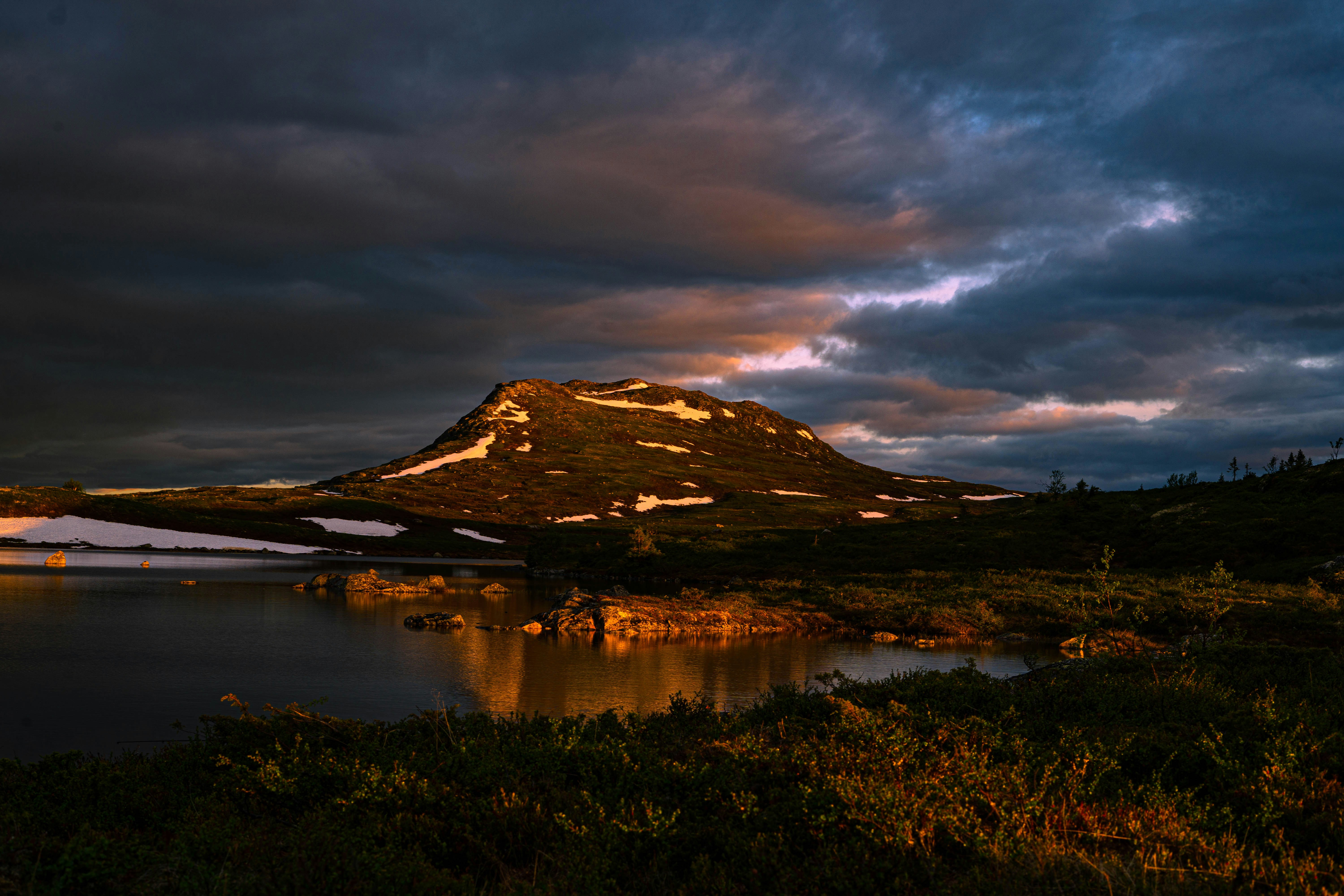 une montagne avec un lac en dessous sous un ciel nuageux