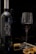 A bottle of wine labeled 'PIACERE' stands next to a filled wine glass. The setting includes wine corks, a corkscrew, and scattered walnuts on a reflective surface.