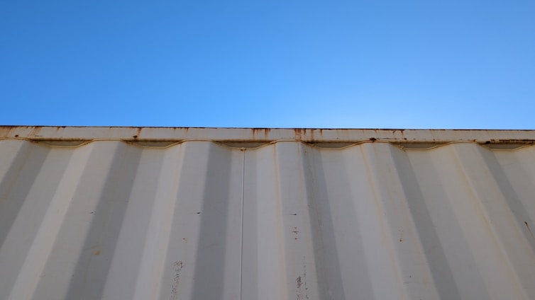A sturdy 40-foot shipping container with double doors open, set against a clear blue sky at an industrial site.