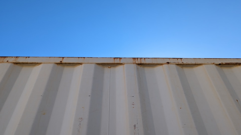 A sturdy 20-foot shipping container painted deep blue, set on a gravel lot under a bright sky.