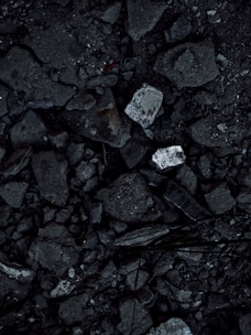 A close-up view of a surface covered in dark, rough asphalt with scattered pieces of white rubble and debris. The texture is uneven and consists of various-sized stones and broken concrete fragments.