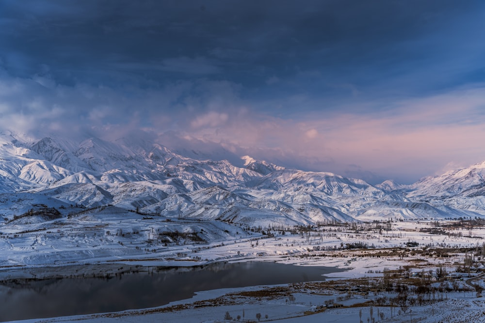 a snow covered mountain range with a lake in the foreground