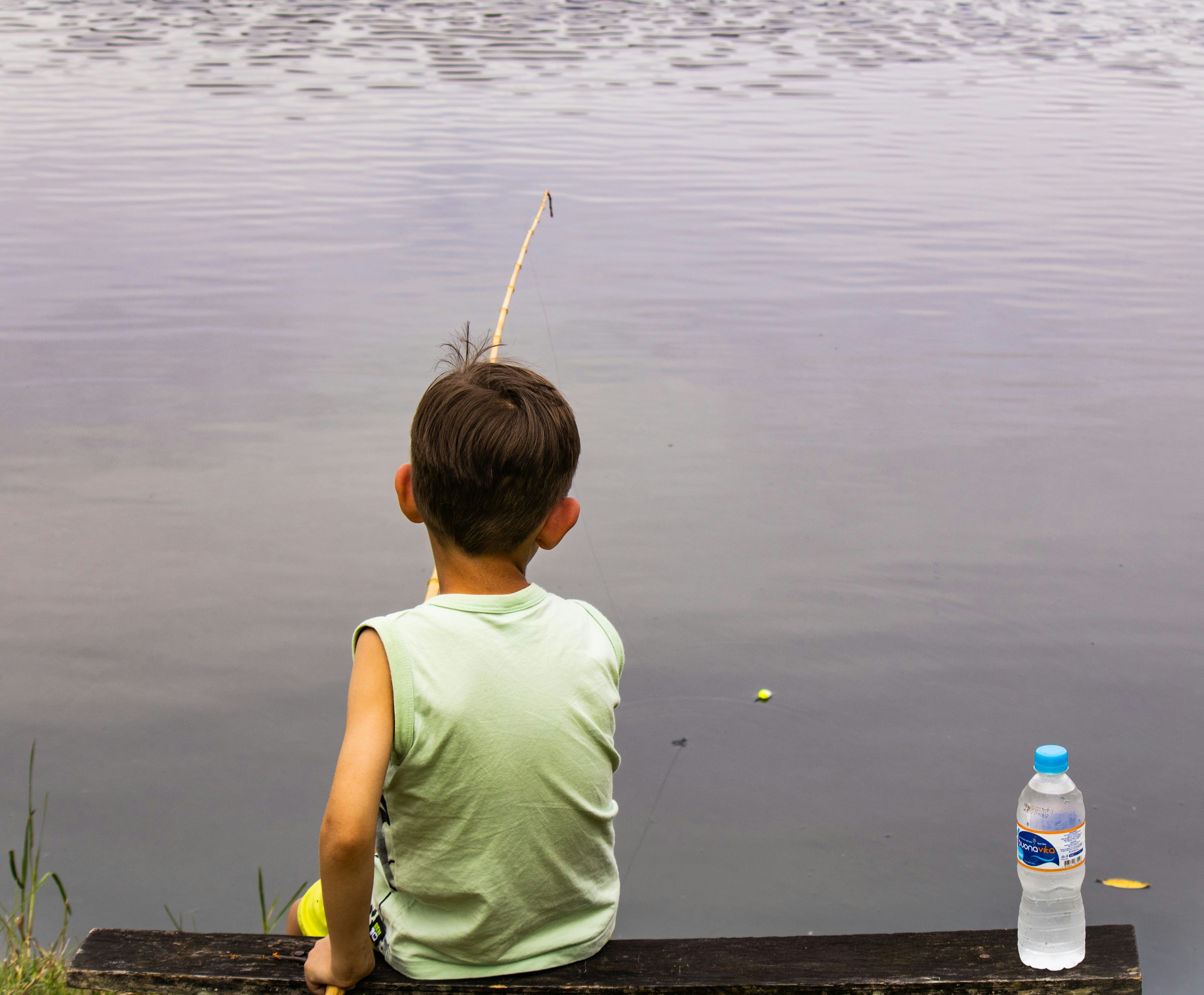 a young boy sitting on a bench next to a body of water