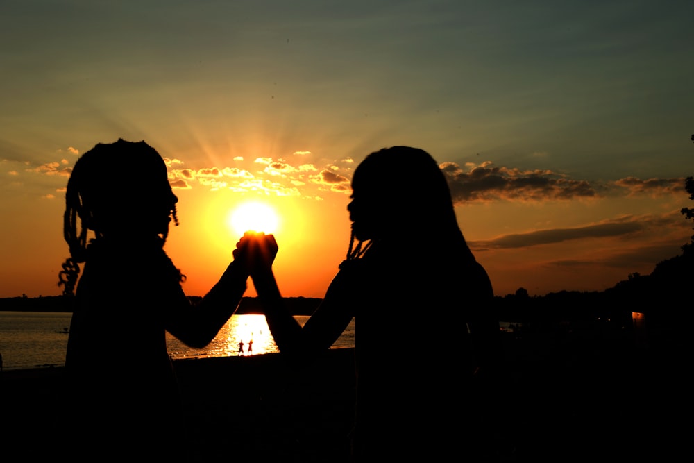 two women standing next to each other in front of a sunset