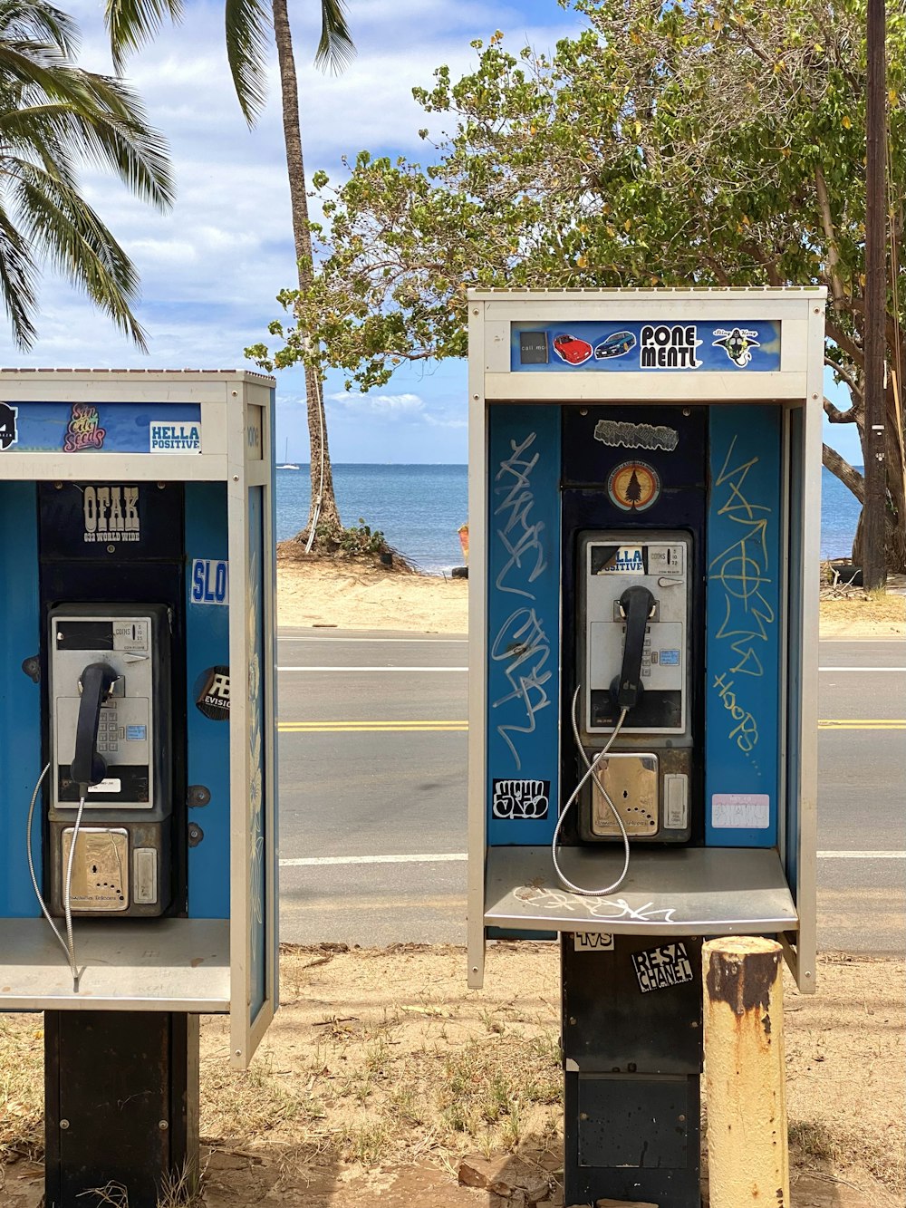 two old style pay phones sitting on the side of the road