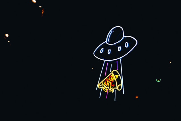 Neon lights create the image of a UFO beaming up a slice of pizza against a dark background.