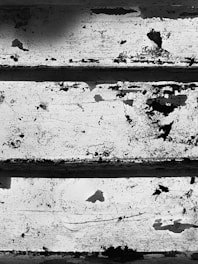 Peeling paint and rust on a set of worn metal stairs. The surface features cracks and spots of corrosion, creating a rough and textured appearance.