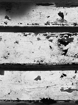Peeling paint and rust on a set of worn metal stairs. The surface features cracks and spots of corrosion, creating a rough and textured appearance.
