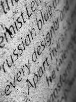 Close-up view of black text in varying fonts and sizes on a textured, light-colored surface. The background appears to be grainy, enhancing the contrast and making the text stand out.