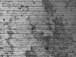 A textured surface with a series of horizontal grooves and organic staining. The material appears to be concrete or a similar substance, with dark patches indicating weathering or wear.