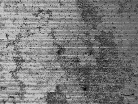 A textured surface with a series of horizontal grooves and organic staining. The material appears to be concrete or a similar substance, with dark patches indicating weathering or wear.