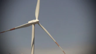 A dynamic shot of a wind turbine spinning against a clear blue sky, with a power station visible in the background.