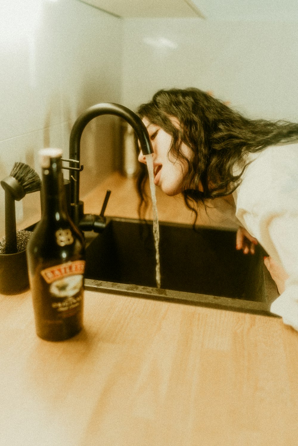 a woman drinking water from a kitchen sink