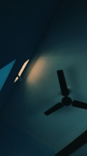 An electrician installing a ceiling fan in a bright living room.