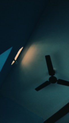 An electrician installing a ceiling fan in a bright room.