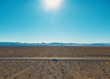 A desert tractor operator carefully spreading gravel on a driveway under a bright sky.