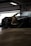 A sleek, modified sports car with exposed engine components is parked inside a garage. The vehicle has a dark exterior with visible aerodynamic elements, such as a significant body kit. Parts of the hood are removed, revealing intricately designed metal pipes and components.
