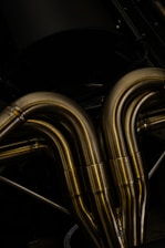 A close-up view of metallic pipes with a smooth, curved design. The pipes appear to be made of polished metal, reflecting light and showcasing a shiny surface.
