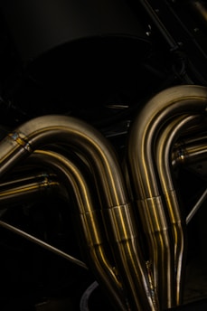 A close-up view of metallic pipes with a smooth, curved design. The pipes appear to be made of polished metal, reflecting light and showcasing a shiny surface.