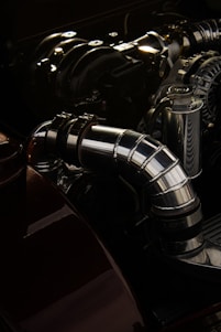 A detailed view of a polished metal component, likely part of an engine or machinery, with various interconnected parts and tubes. The metallic surfaces are shiny and reflect light, creating a smooth and industrial aesthetic.