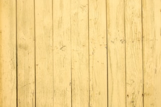 A series of vertical wooden planks with a distressed yellow paint finish. The surface shows visible grain patterns and imperfections, creating a rustic, aged appearance.