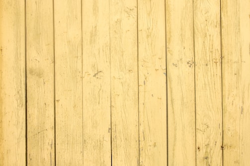 A series of vertical wooden planks with a distressed yellow paint finish. The surface shows visible grain patterns and imperfections, creating a rustic, aged appearance.