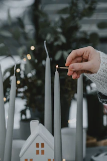 A hand lighting a belongco candle, surrounded by soft white and yellow decor.