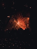 A vibrant display of laser lights creates an array of red and orange beams radiating across a dark background. Silhouettes of people stand in the foreground, looking towards the light display.