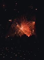 A vibrant display of laser lights creates an array of red and orange beams radiating across a dark background. Silhouettes of people stand in the foreground, looking towards the light display.