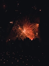 A vibrant display of laser lights creates an array of red and orange beams radiating across a dark background. Silhouettes of people stand in the foreground, looking towards the light display.
