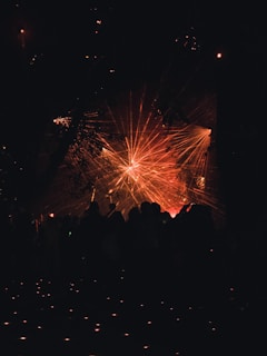 A vibrant display of laser lights creates an array of red and orange beams radiating across a dark background. Silhouettes of people stand in the foreground, looking towards the light display.