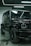A luxury black SUV is parked indoors, surrounded by a modern industrial setting with sleek black and metallic surfaces. Overhead lights create reflective highlights on the vehicle's glossy surface, and the large tires and distinctive front grille are prominently displayed.