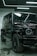 A luxury black SUV is parked indoors, surrounded by a modern industrial setting with sleek black and metallic surfaces. Overhead lights create reflective highlights on the vehicle's glossy surface, and the large tires and distinctive front grille are prominently displayed.