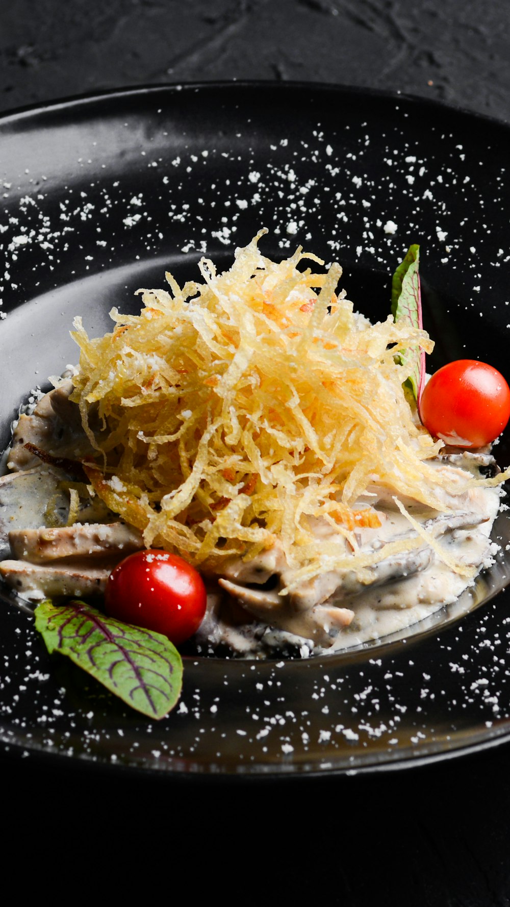 a black plate topped with pasta and tomatoes