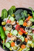 a black bowl filled with vegetables on top of a wooden table