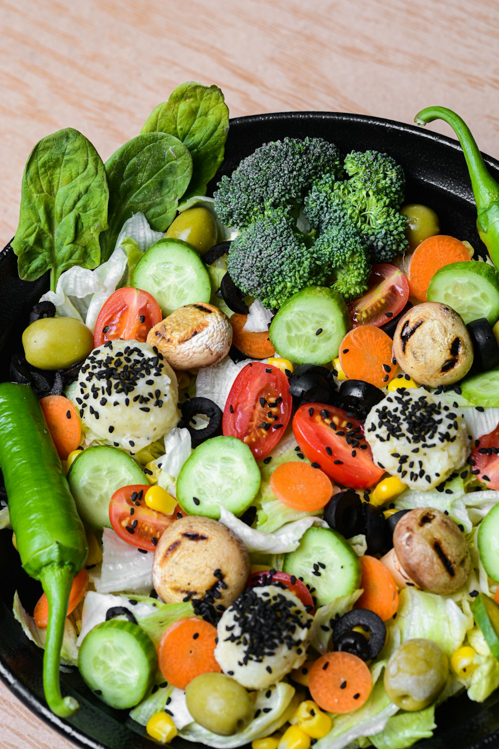 a black bowl filled with vegetables on top of a wooden table