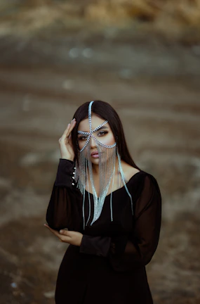 A moody, editorial-style shot of a model wearing multiple micro-welded chains around her neck, set against a deep forest green backdrop.