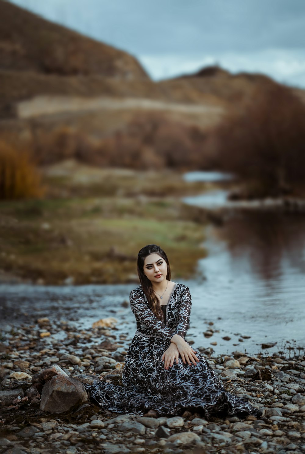 a woman sitting on a rocky beach next to a body of water
